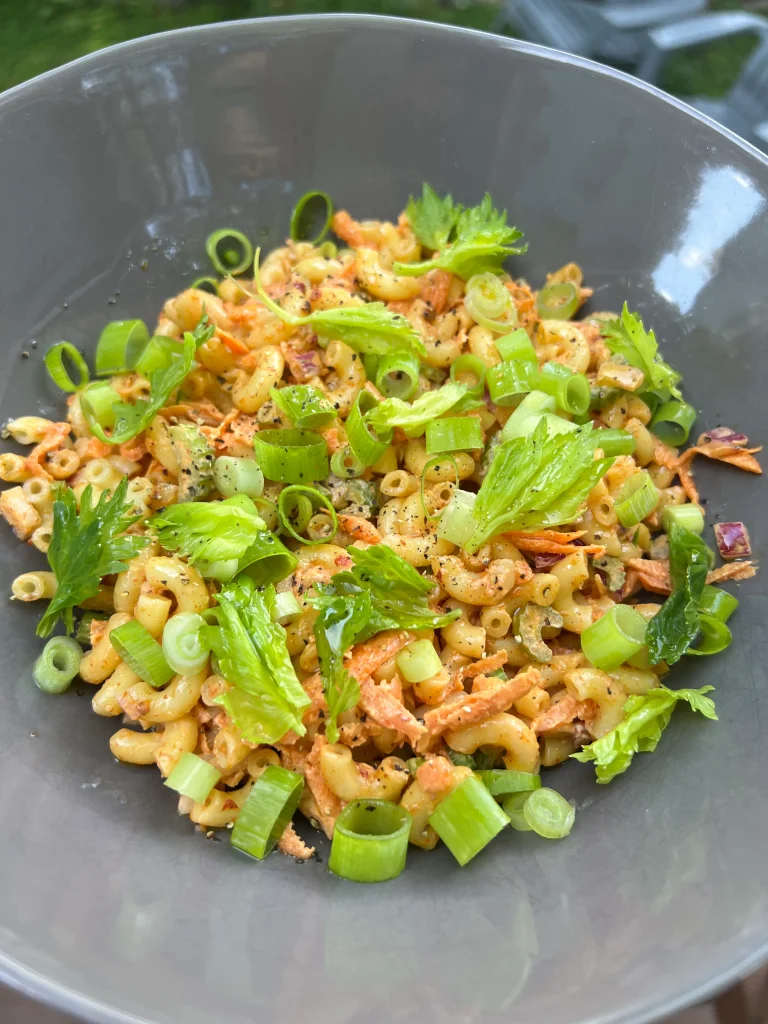Homemade macaroni salad with pops of color from celery leaves and shredded carrots