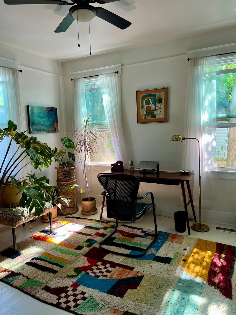Photo of a therapy office, showing a desk, laptop, chair, and various plants and hung pictures. 